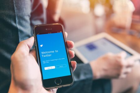 Twitter App on iPhone with people using tablet background closeup male hand hold social network on smart device concept. 23 September 2018, Bangkok Thailand.のeditorial素材