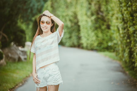 asian thin hipster girl wearing sunglasses walking in the green park relax holiday vintage color toneの写真素材