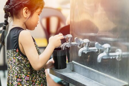 little girl drinking water from public cooling tank water tap good for healthy and stay hydrated in the heat summer season, 21 October 2018, Bangkok, Thailand.のeditorial素材