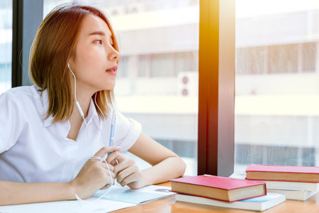 cute young teen Asian university girl in uniform reading book in library