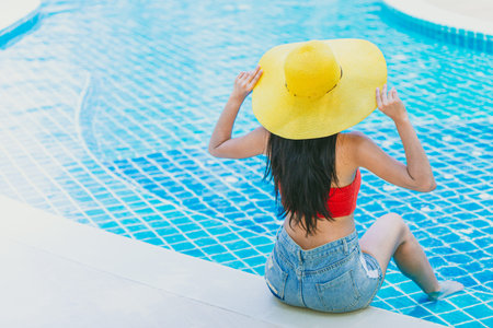 hot girl bikini with hat sitting at hotel swimming pool in summer season vacation holiday