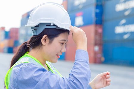 Asian girl teen worker in shipping cargo port work and manage import export goods containers safety with white helmet.の写真素材