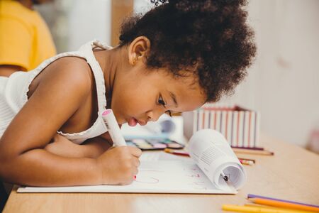 Closeup little child girl black skin writing doing homework at home.の写真素材