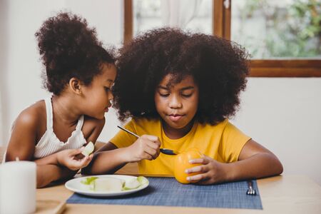 Little cute younger sister looking interesting her older sister try to learning eating vegetable.の写真素材