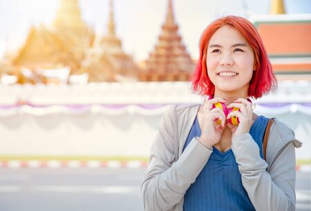Portrait Thai Asian girl new generation young pop teen dyed red hair color shade smiling with Thailand temple background.の写真素材