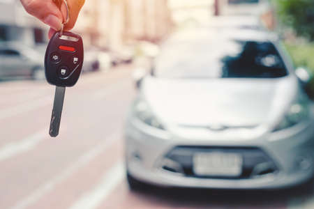 Closeup car key with security remote control button with blur vehicle background for rent drive a car or buy a new car concept.の写真素材