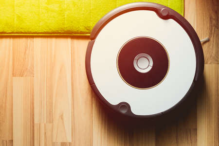 Robot vacuum cleaner on laminate wood floor with carpet cleaningの写真素材