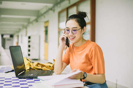 University girl teen using phone call talking with friend while working in campusの写真素材