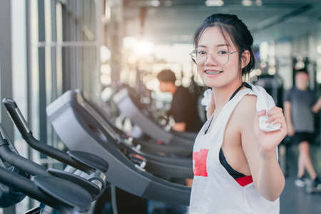 Asian teenage braces girl cardio training exercise in sport club with towel on her shoulders smiling after workout on treadmill in the gym looking camera.の写真素材