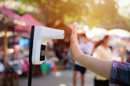 People using infrared contactless temperature assessment devices for measuring body temperatures COVID-19 flu screening at the entranceの写真素材