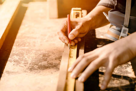 Carpenter man working in furniture wood workshop, Closeup hand measuring and mark on wooden piece.の写真素材
