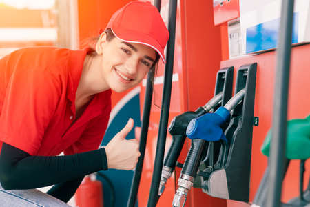 Gas station women worker staff Thumbs up at fuel nozzle dispensers happy service working refill cars gasolineの写真素材