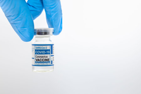 Closeup hand holding Covid Vaccine dose bottle with white space for text.