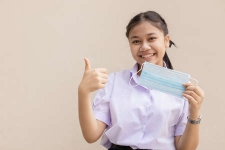 Asian cute student in uniform happy with face mask thumbs up for good health.の写真素材