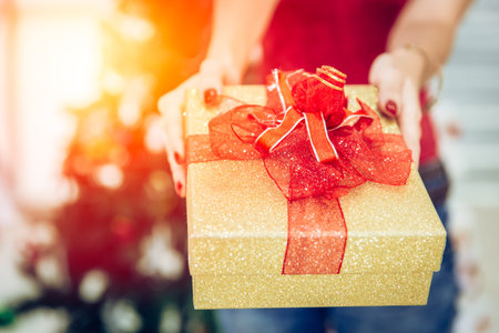 Closeup girl hand giving luxury gold gift box present for new year celebration.