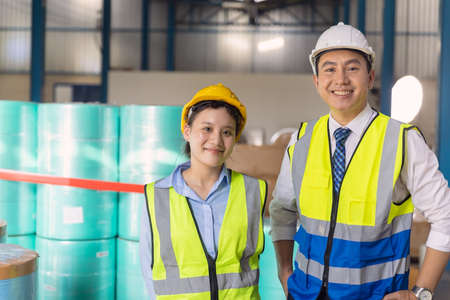 Young engineer working woman standing with adult man worker with safety suit hardhat in factory backgroundの写真素材