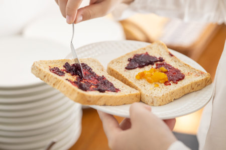 hand apply sweet berry fruit jam on a sliced whole wheat bread for breakfast high energy meal in the...