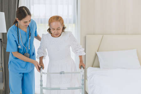 Asian elderly senior woman using walker aid with nurse care support step walking at home.の写真素材