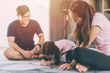 Asian family parents playing with daughter in living room together child drawing cartoon in paper.の写真素材