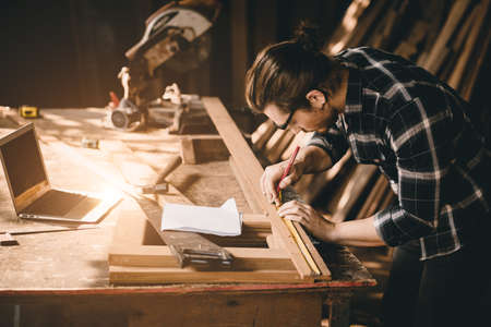 Carpenter man Wood worker working hand made furniture in shop factory industry. male wooden craftsman builder working in workshop with computer aided design.の写真素材