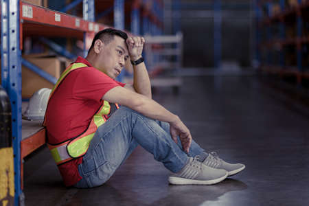 Tired stress Asian male worker labor hard working fatigue sitting resting in warehouse cargo inventory industry.の写真素材