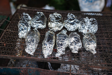 fish or potato wrapped covering with aluminium foil paper grilling on charcoal stoveの写真素材