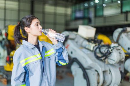 health care woman worker drinking clean water while working in factory machine warehouse for refresh and personal healthyの写真素材