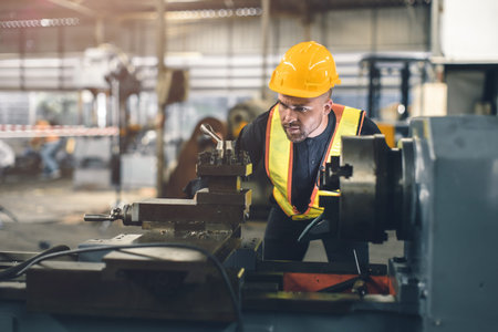 young engineer male worker work in heavy metal industry CNC lathe machine with safety