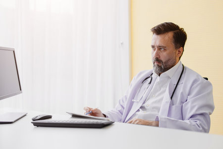 Senior professional doctor male in hospital room working at table listening patient looking stressの写真素材