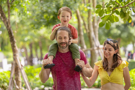 Happy family together walking in public green park young boy sitting on father shoulder around fresh ecology trees environment.の写真素材