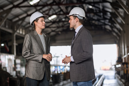 business man and woman standing together talking in heavy industry locomotive shop building site.の写真素材