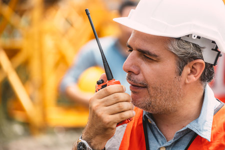 Senior construction engineer worker control operate construction site with radio communication. Foreman order crane tower working by walkie talkie radio.の写真素材