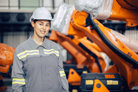 Portrait happy smiling engineer woman standing in robotic factory. Indian female staff worker at robot arm assembly plant.の写真素材