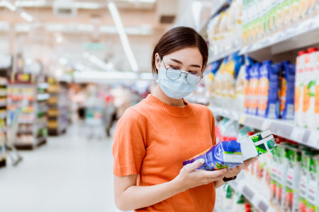 Asian women teen girl with face mask shopping in super market looking compare reading products detail.の写真素材
