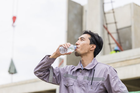 Asian worker male thirsty drinking water in hot summer weather working outdoor at construction siteの写真素材