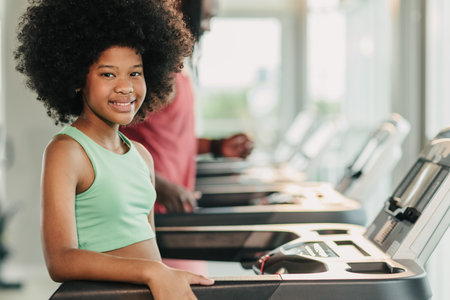 Portrait happy smiling African black healthy kid, Girl child at fitness sport club treadmill machineの写真素材