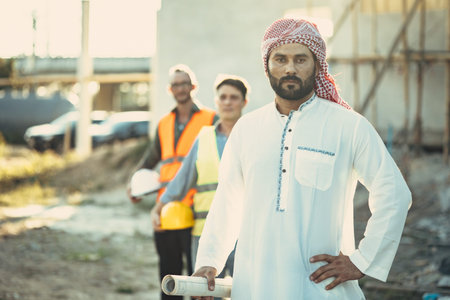 Arab construction engineer architect, Muslim builder working outdoor at construction site with floor plan cooperate with staff workerの写真素材