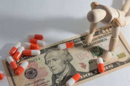 Wooden jointed doll kneeling down and pill on dollarの写真素材