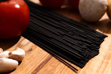 black raw spaghetti and vegetables on a wooden surfaceの写真素材