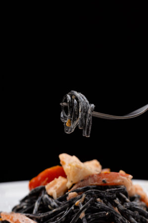 spaghetti with cuttlefish ink and seafood dish on a plate black spaghetti pieces if ribeye shrimps red fish salmon fish spaghetti with seafood macro photo close-up photo spaghetti on a forkの写真素材