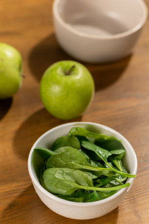 Fresh spinach and green apples in bowls on a wooden tableの写真素材