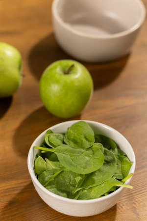 Fresh spinach and green apples in bowls on a wooden tableの写真素材