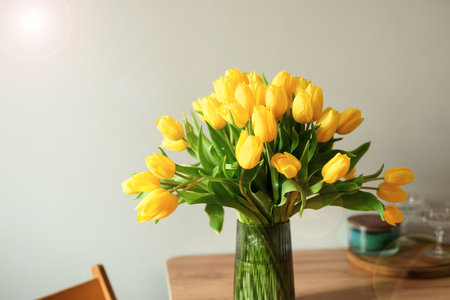 Bright yellow tulips in a vase. Bouquet in a glass vase on the wooden table, light background. Spring home decoration, fresh bouquet of flowers. springtime. Fresh flowers with theの写真素材