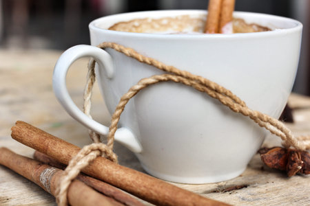 Cup with hot cappuccino with spices cinnamon sticks and star anise.