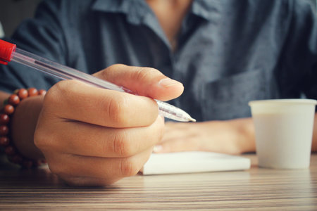 Woman with pen writing on paper and coffee cup