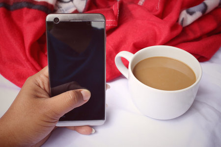 Smart phone with coffee cup on the bed