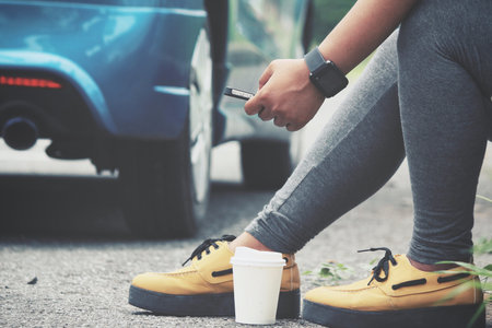Woman using smart phone and coffee paper cup with car on road