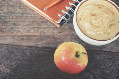 Apple and blank notepad with coffee on office tableの写真素材