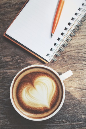 Blank notepad and pen with latte art coffee on office tableの写真素材