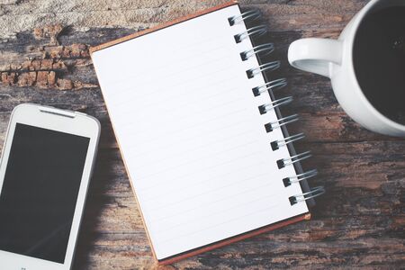 Blank notepad and smart phone with hot coffee on office tableの写真素材